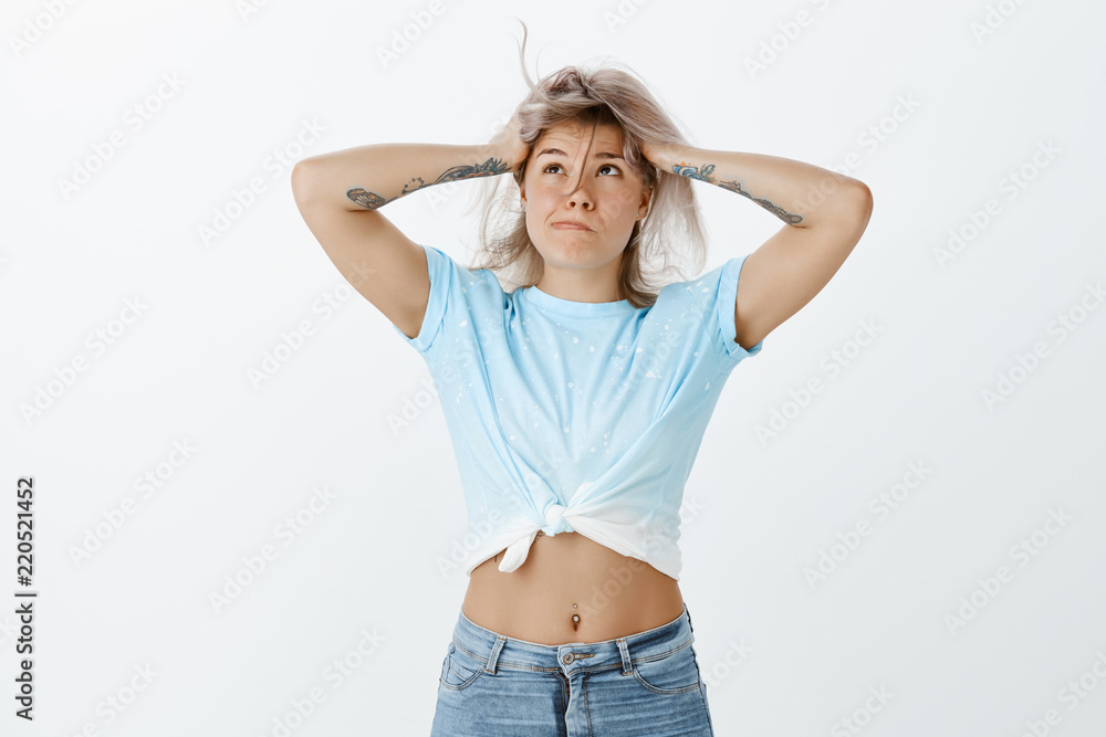 My head gonna blow from information. Pressured tired cute and funny woman  in stylish cropped top and jeans, blowing hair strand off from face,  touching head, sulking, feeling depressed and exhausted Stock