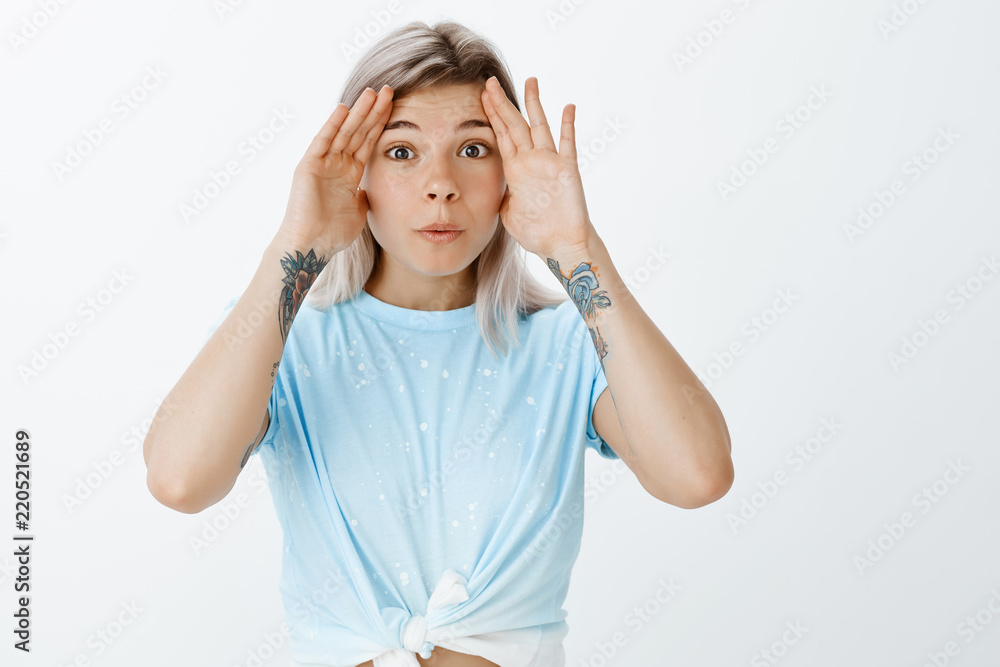 Knock knock. Portrait of charming playful female student in cropped top with tattooed arms, holding palms near fave and folding lips, playing with younger sister or fooling around from boredom Knock knock. Portrait of charming playful female student in cropped top with tattooed arms, holding palms near fave and folding lips, playing with younger sister or fooling around from boredom