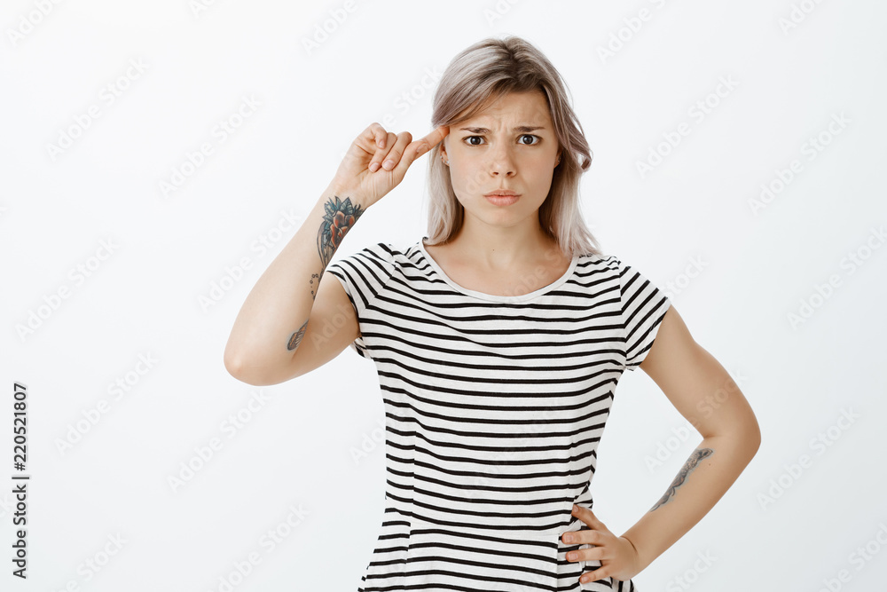 Are you out of mind. Frustrated displeased woman in striped t-shirt, holding hand on hip, rolling index finger over temple and gazing intense at camera, being shocked with crazy idea of friend Are you out of mind. Frustrated displeased woman in striped t-shirt, holding hand on hip, rolling index finger over temple and gazing intense at camera, being shocked with crazy idea of friend