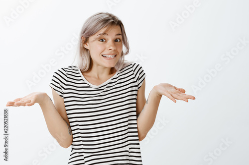 I have no idea really. Carefree cute fair-haired young woman in striped t-shirt shrugging and spreading palms aside while smiling with innocent expression, being unaware and clueless what happened
