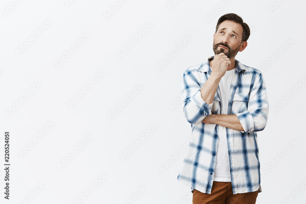 Charming and creative adult poet creating new poem while walking near lake, looking up with thoughtful expression, thinking, touching beard and holding hands crossed over gray background Charming and creative adult poet creating new poem while walking near lake, looking up with thoughtful expression, thinking, touching beard and holding hands crossed over gray background