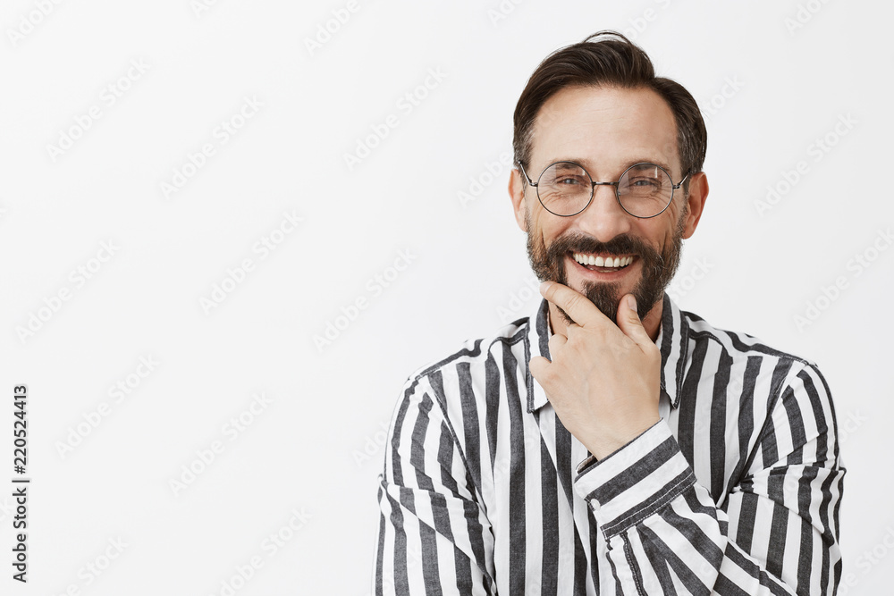 Fototapeta premium Great suggestion, nice work. Satisfied and pleased friendly-looking businessman in glasses, rubbing beard and smiling broadly while gazing with impressed and pleased expression at great project