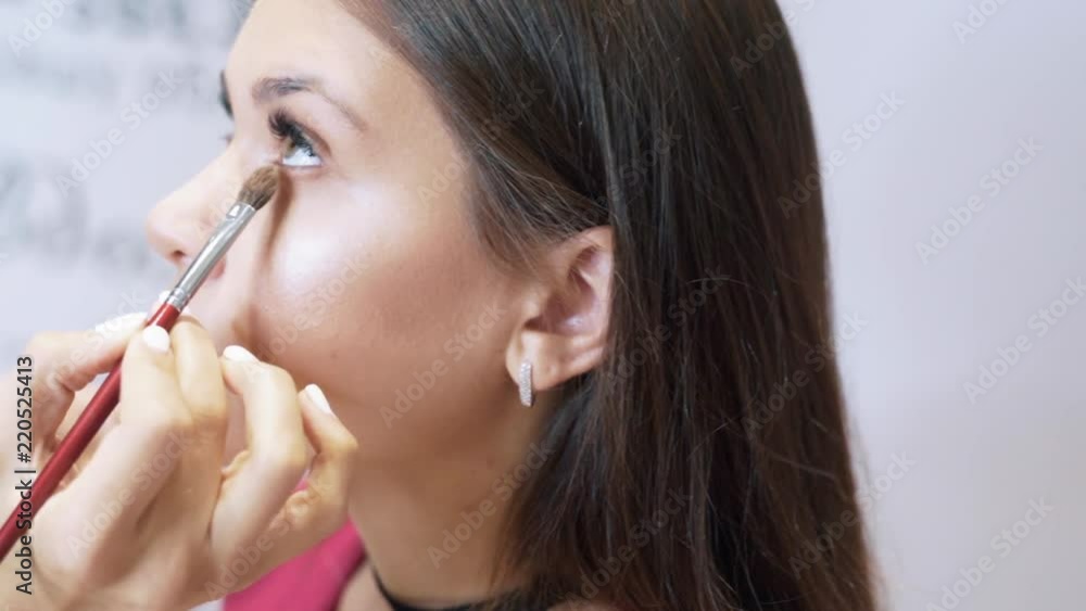Close-up of cropped frame creating natural make-up. The stylist paints the models of the lower eyelid with beige shadows. The concept of beauty salons, make-up, feminine image, beauty, cosmetics. Close-up of cropped frame creating natural make-up. The stylist paints the models of the lower eyelid with beige shadows. The concept of beauty salons, make-up, feminine image, beauty, cosmetics.