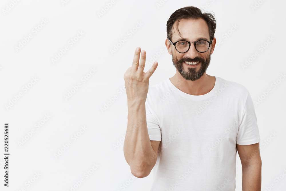 Man have three cars in garage, bragging about sucessful and rich life. Portrait of stylish good-looking mature male model in glasses with beard showing third number with fingers and smiling carefree Man have three cars in garage, bragging about sucessful and rich life. Portrait of stylish good-looking mature male model in glasses with beard showing third number with fingers and smiling carefree