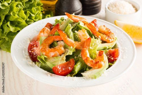 Fresh Caesar shrimp salad with delicious prawns, ruccola, spinach, cabbage, arugula, egg, parmesan and cherry tomato on wooden background. Oil, salt and pepper. Healthy and diet food concept.