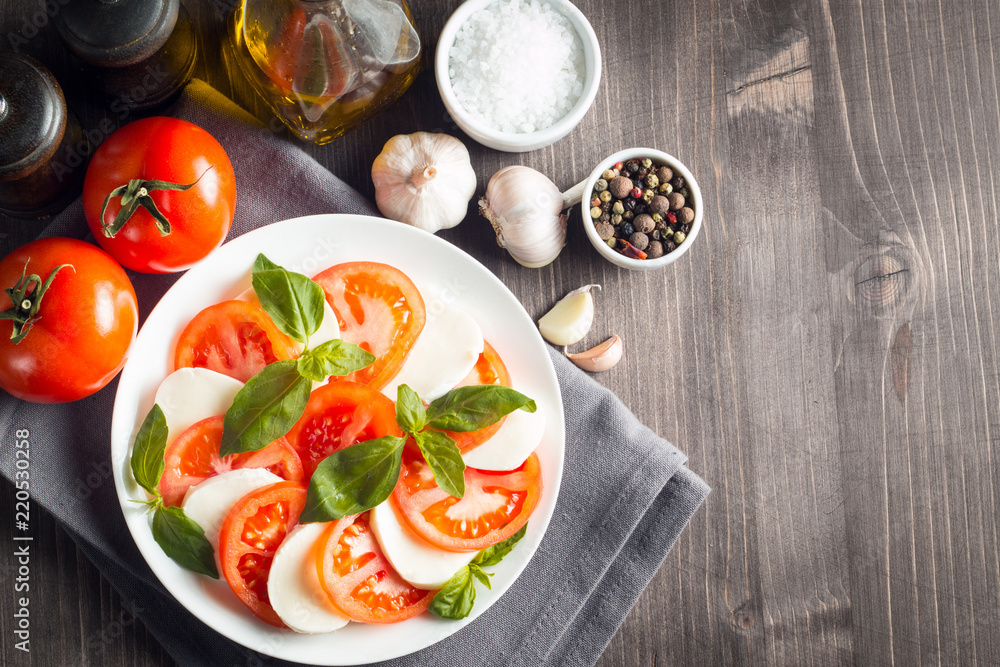 Photo of Caprese Salad with tomatoes, basil, mozzarella, olives and olive oil on wooden background. Italian traditional caprese salad ingredients. Mediterranean, organic and natural food concept.