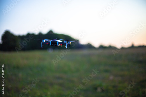 White flying drone on a background of green field and trees
