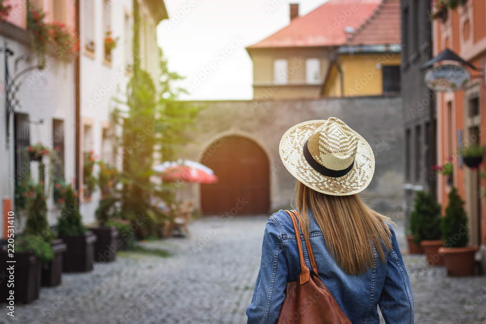 Woman wearing jeans jacket and straw hat. Tourist walking in the streets of European city 
