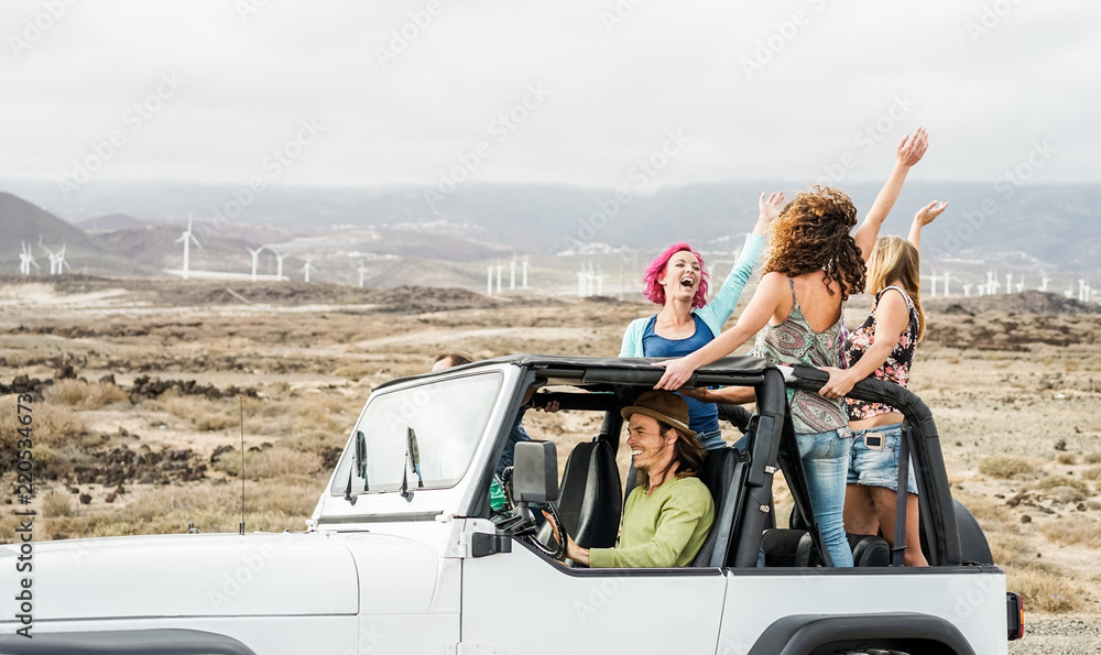 Happy tourists friends doing excursion on desert in convertible 4x4 car