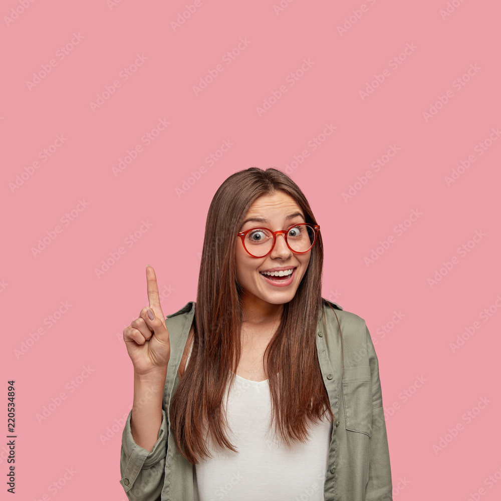 Smiling happy emotional sensitive Caucasian student graduated from universirty, raises fore finger and show blank space upwards, dressed in fashionable clothes, isolated over pink background. Smiling happy emotional sensitive Caucasian student graduated from universirty, raises fore finger and show blank space upwards, dressed in fashionable clothes, isolated over pink background.