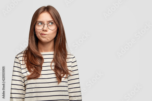 Well, I dont know. Doubrtful thoughtful beautiful woman purses lips, has indecisive expression, being deep in thoughts, isolated over white background with copy space for your promotion or slogan