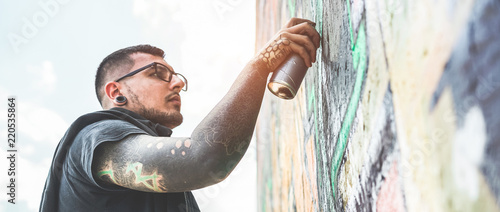 Photography Tattooed graffiti writer painting with color spray his picture on the wall