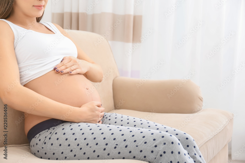 Pregnant woman holding hands on belly indoors Pregnant woman holding hands on belly indoors