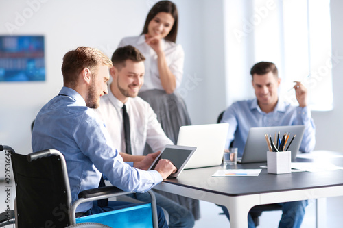 Young man in wheelchair with colleagues at workplace