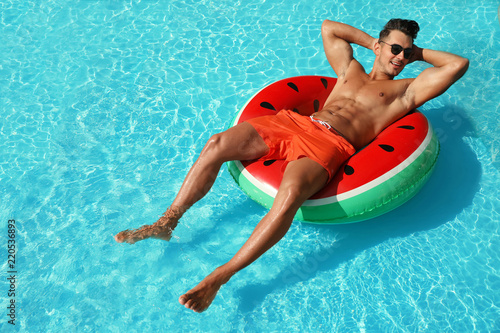 Young man with inflatable ring in pool on sunny day