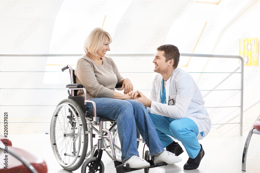Male doctor taking care of mature woman in wheelchair indoors Male doctor taking care of mature woman in wheelchair indoors