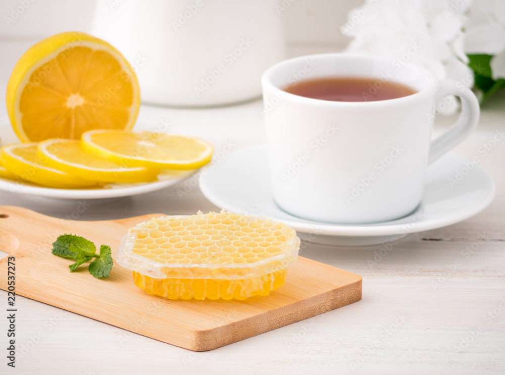 White Cup with tea, lemon slices and honey in honeycomb on white wooden table, side view White Cup with tea, lemon slices and honey in honeycomb on white wooden table, side view