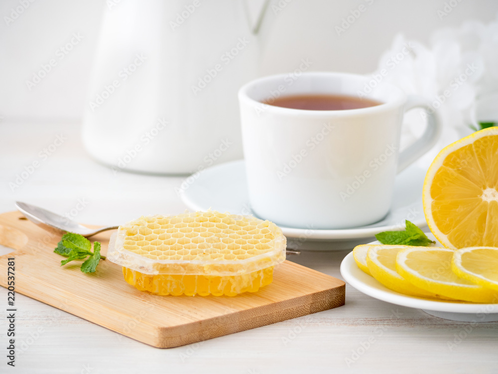 White Cup with tea, lemon slices and honey in honeycomb on white wooden table, side view White Cup with tea, lemon slices and honey in honeycomb on white wooden table, side view