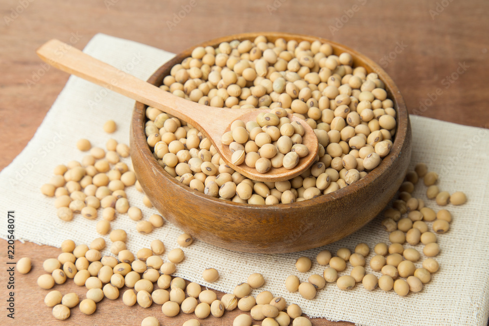 Soybeans in wooden bowl and spoon putting on linen and wooden background.