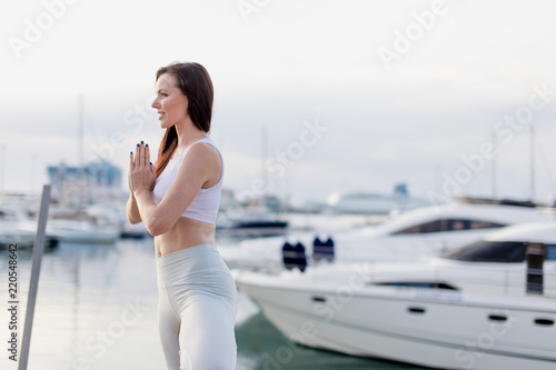 Woman meditating in yoga tree pose at marine, motor seaboats, Motivation and inspirational fit and exercising. Healthy lifestyle outdoors at seaside, fitness concept. photo