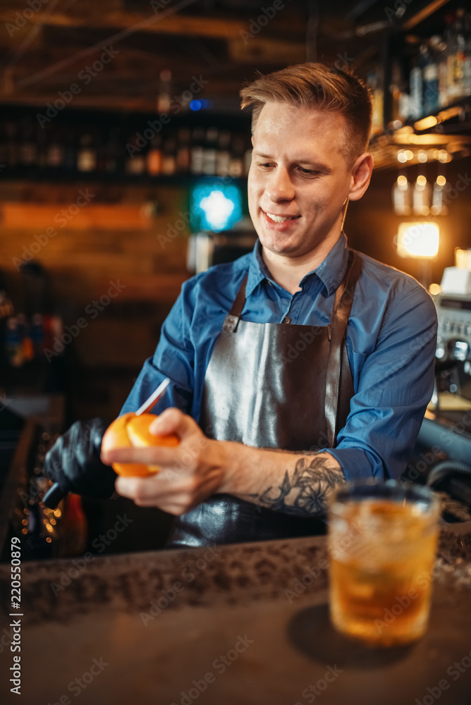 Male bartender cleans orange at the bar counter