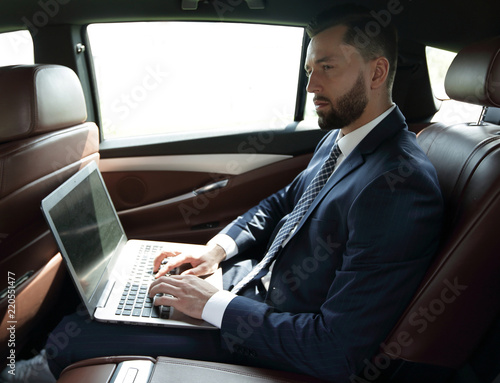 businessman using a laptop in the backseat of a car