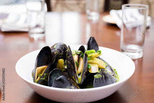 Mussels in shells in a white bowl with a green sauce on a dining table.