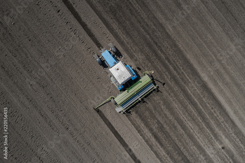 Aerial view of blue tractor plows the earth in field on a summer day against a black earth background. Agriculture. Top view. Pattern