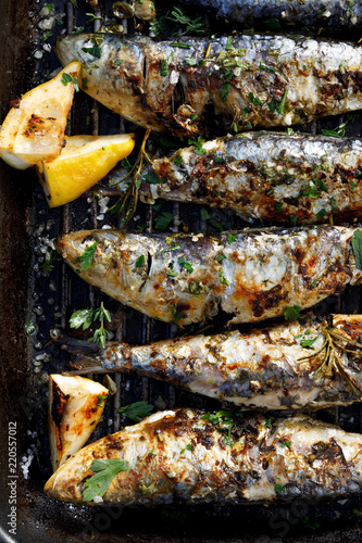 Grilled sardines in a herbal lemon marinade on a grill plate, top view. Grilled seafood, barbecue
