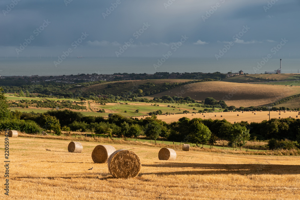 Beautiful Summer landscape of field of hay bales with dramatic stormy clouds overhead in English countryside