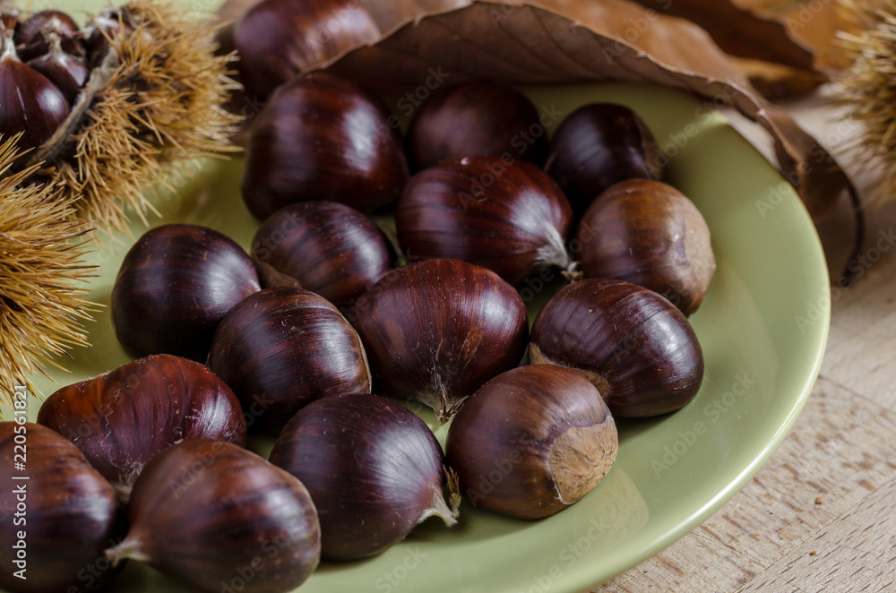chestnuts and autumn feeling, view of a dish full of chestnuts surrounded by husk and leaves. chestnuts and autumn feeling, view of a dish full of chestnuts surrounded by husk and leaves.