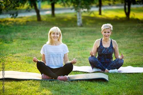 two adult women aged yoga outdoors in summer in the park