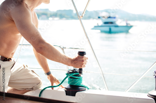 Cropped view of yacht captain working on the boat with winch on a sailboat during the ocean voyage, sailing concept. photo