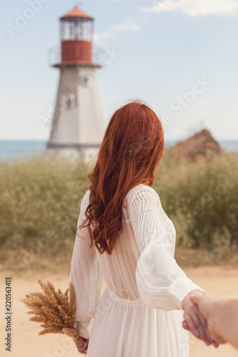 follow me. Beautiful girl with flowers looking at the sea and the lighthouse