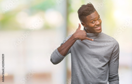 Young african american man over isolated background smiling doing phone gesture with hand and fingers like talking on the telephone. Communicating concepts.