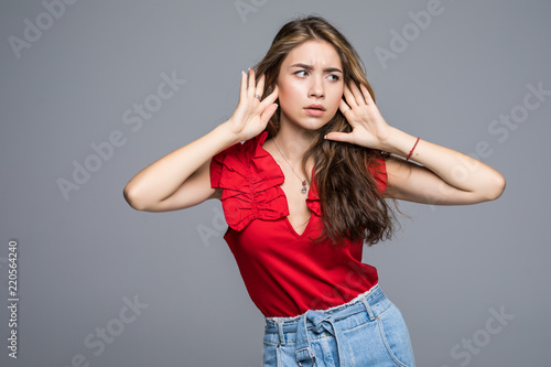 Young woman in casual wear holding hands on head and shouting while standing against gray studio background.