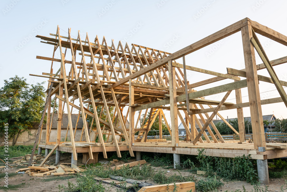 Wooden rafters of a new home under construction at sunset. New house construction interior with exposed framing. Wooden rafters of a new home under construction at sunset. New house construction interior with exposed framing.