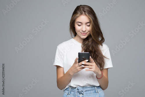 Smiling lovely young woman standing and using phone over grey background