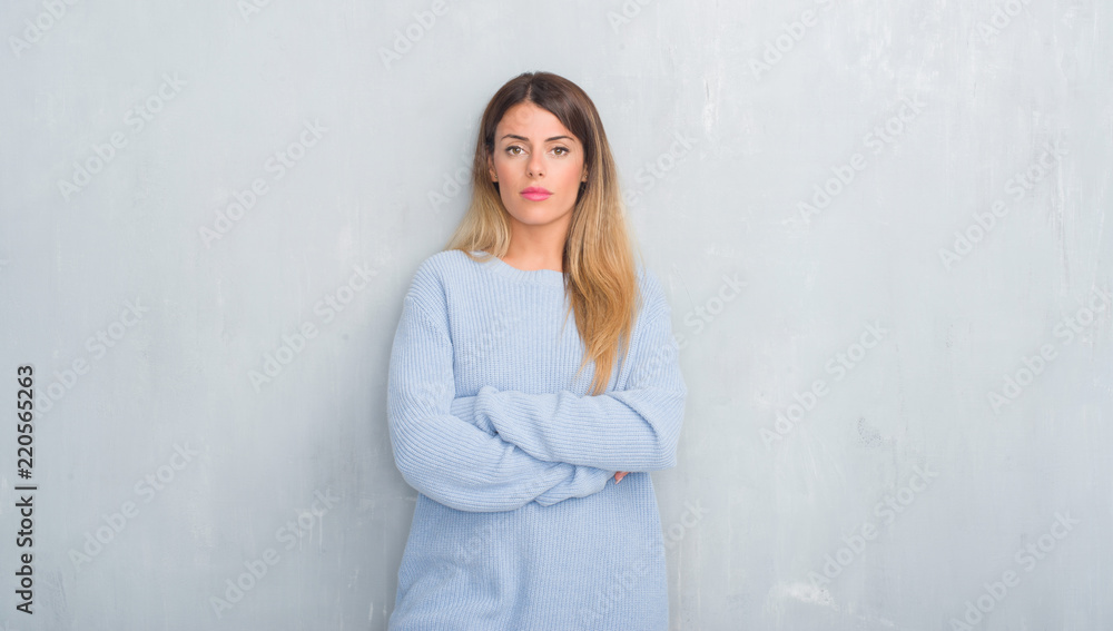 Young adult woman over grey grunge wall wearing winter outfit with serious expression on face. Simple and natural looking at the camera. Young adult woman over grey grunge wall wearing winter outfit with serious expression on face. Simple and natural looking at the camera.