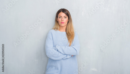 Young adult woman over grey grunge wall wearing winter outfit with serious expression on face. Simple and natural looking at the camera. © Krakenimages.com
