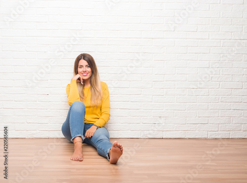Young adult woman sitting on the floor over white brick wall with a happy and cool smile on face. Lucky person. © Krakenimages.com