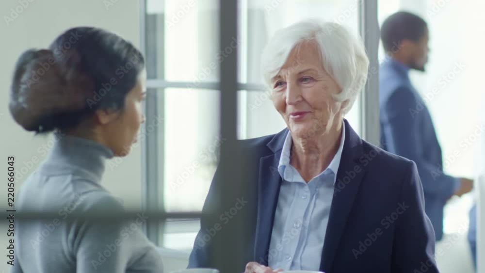 Medium shot of friendly senior woman having relaxed conversation with younger colleague over cup of tea or coffee Medium shot of friendly senior woman having relaxed conversation with younger colleague over cup of tea or coffee