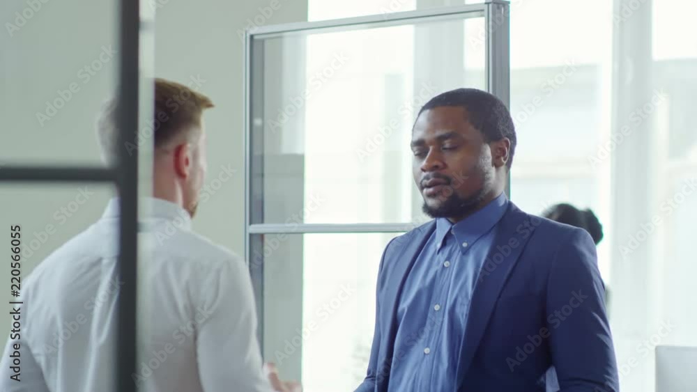Tilt down shot of two friendly multiethnic male colleagues enjoying refreshing coffee or tea and discussing work Tilt down shot of two friendly multiethnic male colleagues enjoying refreshing coffee or tea and discussing work