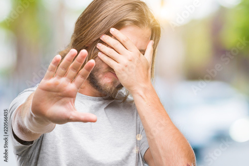 Young handsome man with long hair over isolated background covering eyes with hands and doing stop gesture with sad and fear expression. Embarrassed and negative concept.