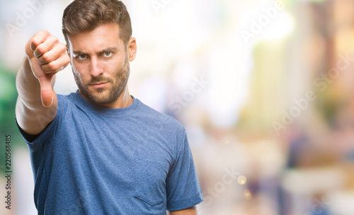 Young handsome man over isolated background looking unhappy and angry showing rejection and negative with thumbs down gesture. Bad expression.
