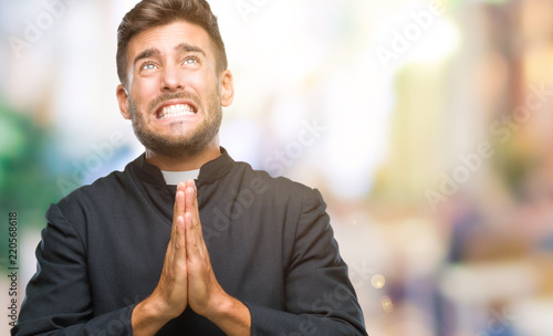 Obraz na plátně Young catholic christian priest man over isolated background begging and praying with hands together with hope expression on face very emotional and worried