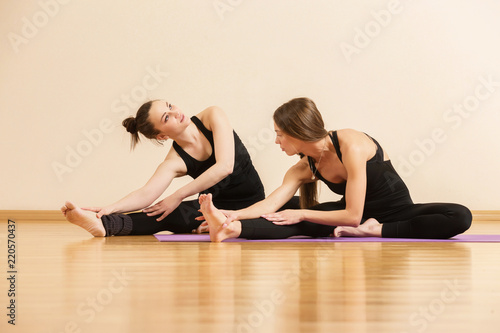 Two young girls are training yoga at gym. Teacher is helping student make asana pose for proper woman health. photo