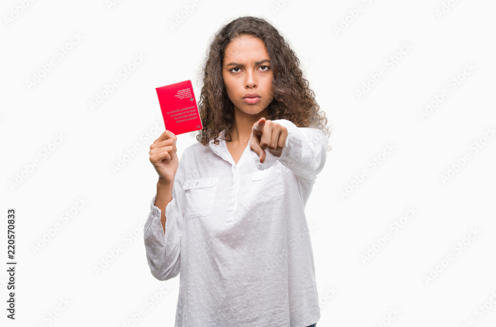 Young hispanic woman holding passport of Switzerland pointing with finger to the camera and to you, hand sign, positive and confident gesture from the front Young hispanic woman holding passport of Switzerland pointing with finger to the camera and to you, hand sign, positive and confident gesture from the front