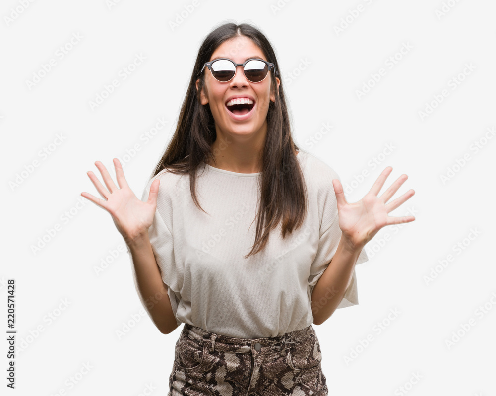 Young beautiful hispanic wearing sunglasses very happy and excited, winner expression celebrating victory screaming with big smile and raised hands Young beautiful hispanic wearing sunglasses very happy and excited, winner expression celebrating victory screaming with big smile and raised hands