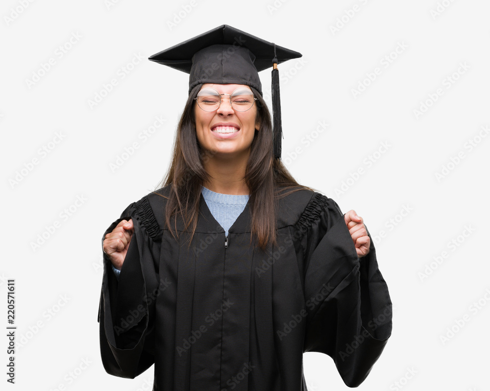Young hispanic woman wearing graduated cap and uniform excited for success with arms raised celebrating victory smiling. Winner concept. Young hispanic woman wearing graduated cap and uniform excited for success with arms raised celebrating victory smiling. Winner concept.